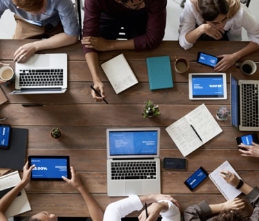 people sitting around a table with laptops phones and notepads